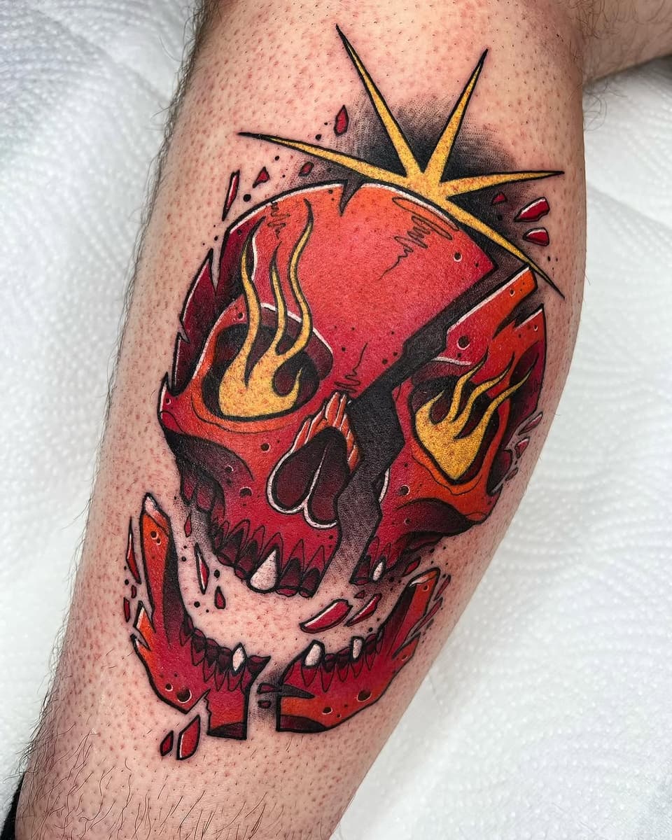 Vibrant red skull with yellow star burst and flames tattoo on the calf, featuring dark shading and detailed linework.