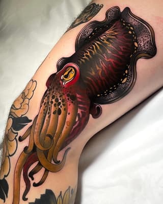 Detailed octopus tattoo on upper arm with tentacles extending downward, featuring warm orange and red tones with black outlines and textured shading.