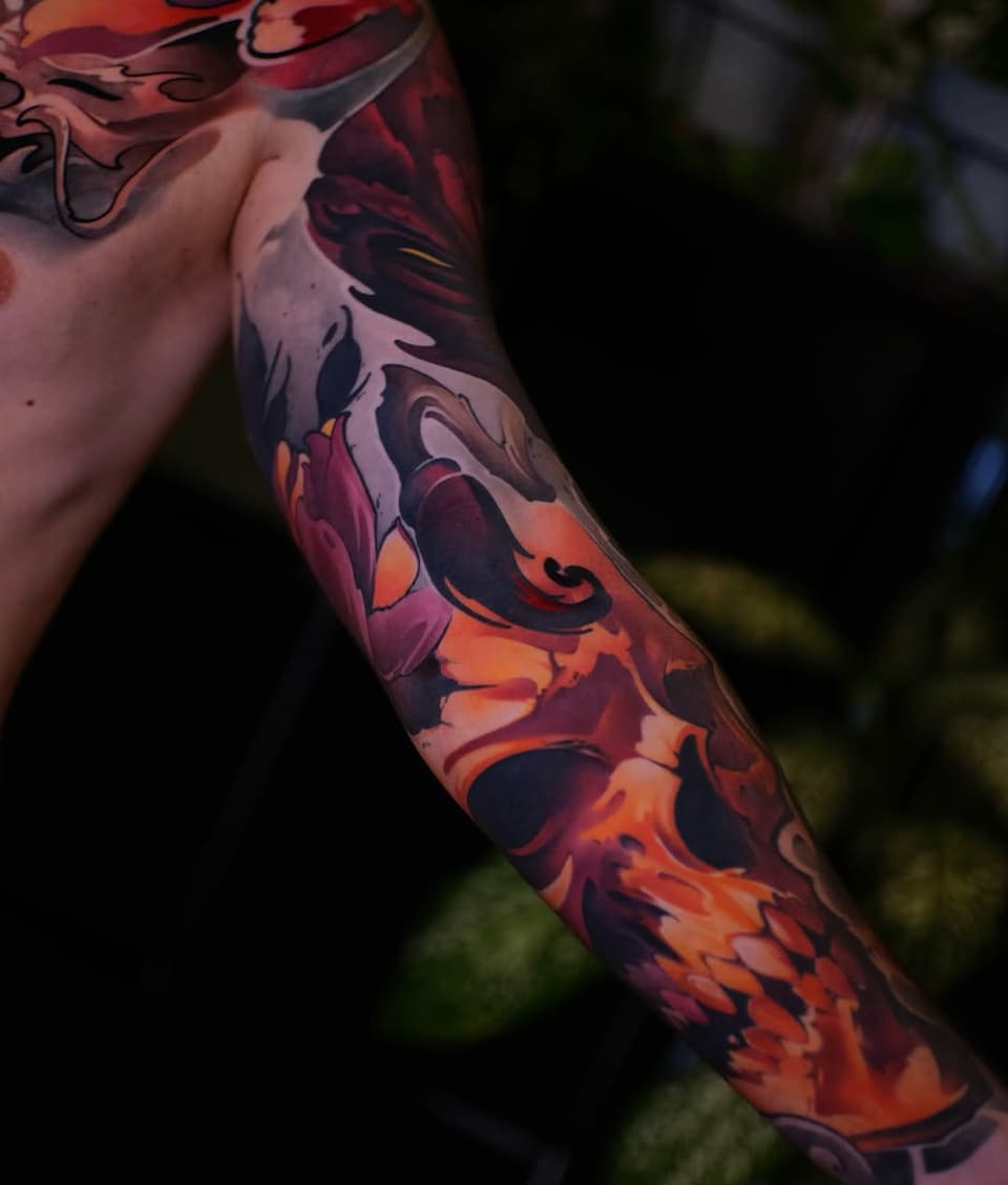 Colorful full-sleeve arm tattoo featuring red, orange, and burgundy floral and ornamental designs with flowing curves and detailed shading.