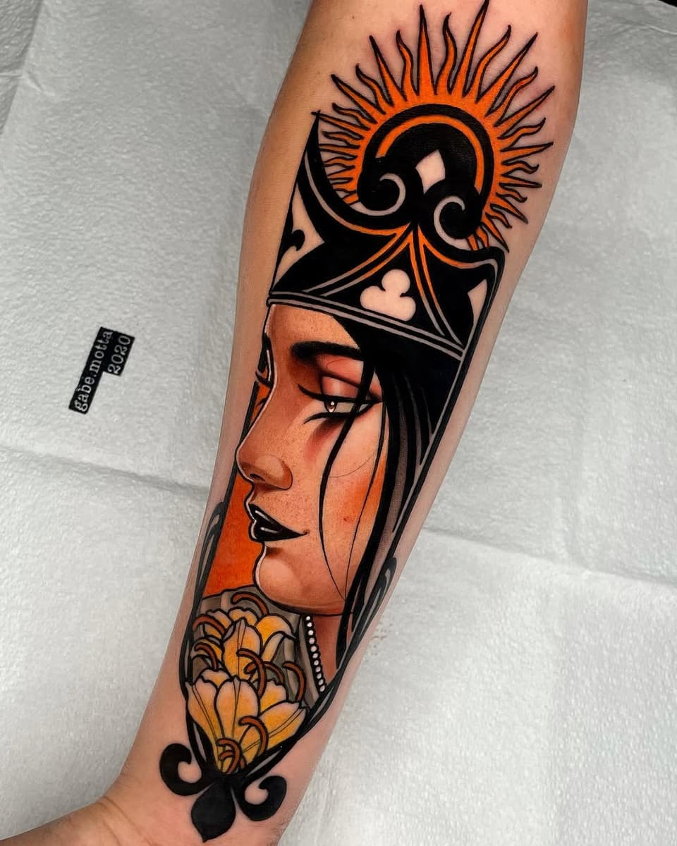 Colorful forearm tattoo featuring a woman's profile with Egyptian headdress, sun symbol above, and golden flowers below, outlined in black with orange and gold accents.