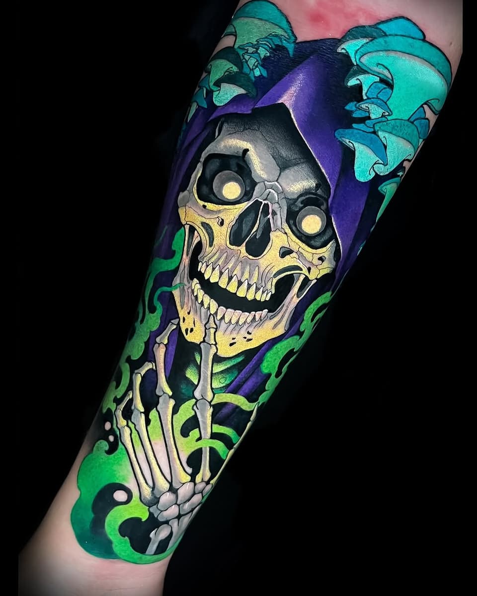 Colorful skull tattoo on forearm featuring yellow bone details, glowing eyes, green and purple flowing background elements, and decorative swirling designs.