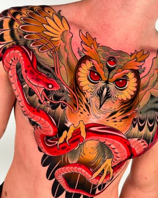 Colorful owl tattoo on chest featuring red snakes, orange and yellow feather details, and bold red eyes with intricate shading.