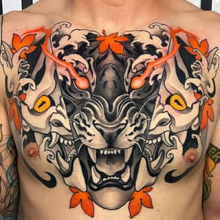Large symmetrical tiger face chest tattoo featuring black shading, orange and yellow floral accents, ornamental scrollwork, and bared fangs.