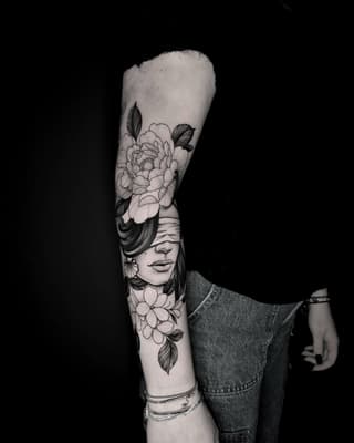 Full arm sleeve tattoo featuring a woman's face with closed eyes surrounded by large peonies and smaller flowers with detailed leaves in black ink.