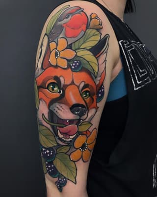 Colorful arm tattoo featuring a red fox's face surrounded by orange flowers, berries, and green leaves, with a robin perched above.