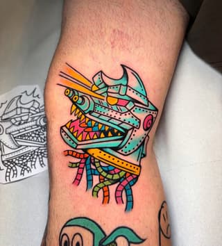 Colorful tattoo on the leg featuring a stylized creature with horns, sharp teeth, and tentacles in turquoise, orange, yellow, and pink.