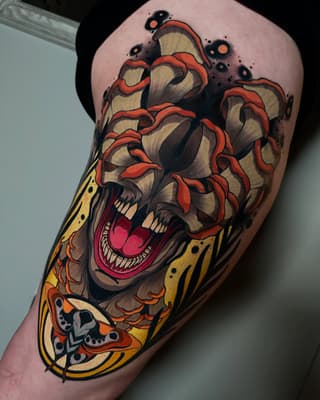 Colorful skull tattoo with red brain-like tendrils, yellow and orange decorative elements, and a moth design on the upper arm.