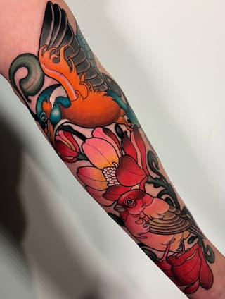 Colorful sleeve tattoo featuring a winged heart, flowering lotus, and bird with orange, red, teal, and black details on the forearm.