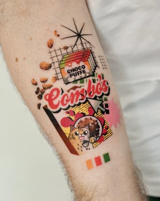 Colorful tattoo on a calf featuring a Choco Puffs cereal box, a cat, the word "Zombies," geometric elements, and scattered cereal pieces.
