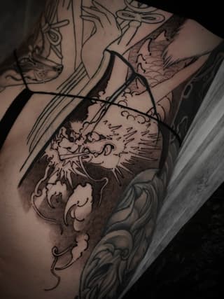 Lion head tattoo with decorative scrollwork and shading on upper arm, shown against a framed mirror or reflective surface.