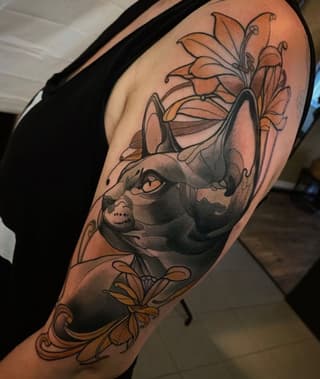 Colorful arm tattoo featuring a cat's face with orange and yellow flowers, surrounded by decorative floral elements and swirling designs.