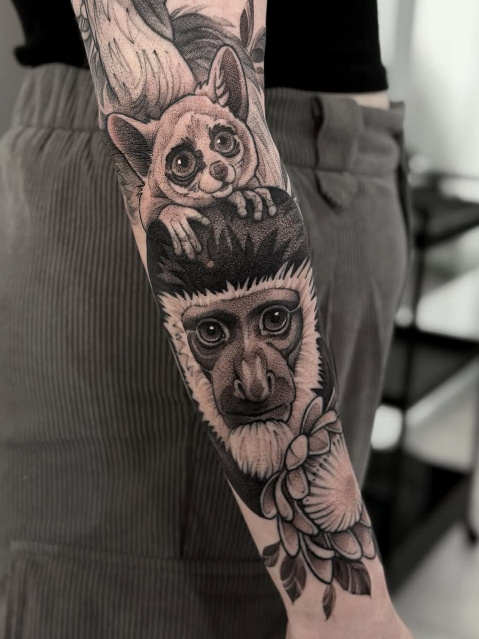 Forearm tattoo featuring three primates with detailed facial expressions and decorative floral elements below, rendered in black and grey ink.