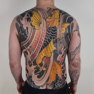 Back tattoo featuring golden winged figures with ornate scrollwork in orange, red, black, and tan colors on a shirtless male torso.