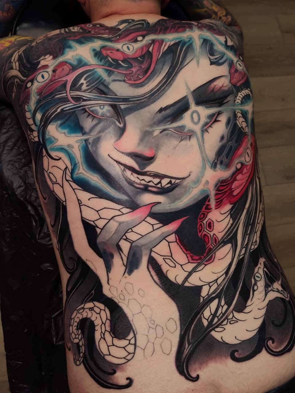 Large back tattoo featuring a smiling face with serpents and tentacles in black, red, pink, and teal colors.