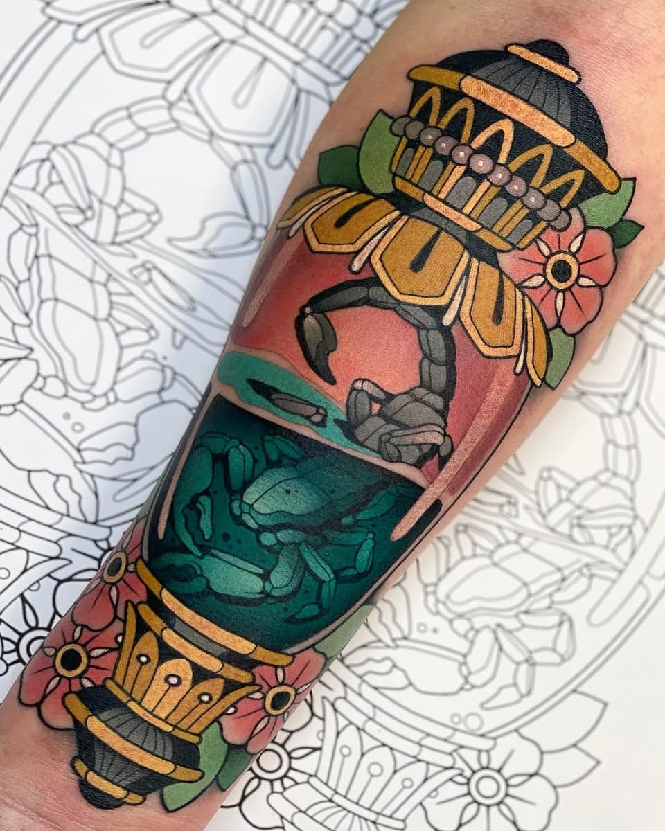 Colorful arm tattoo featuring a stacked crab design with floral elements, gold accents, and a coral-to-teal gradient background on the forearm.