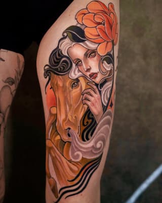 Colorful arm tattoo featuring a woman's face with flowing hair, orange flower above her head, and warm orange and black decorative elements below.