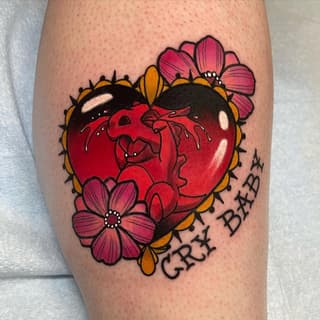Anatomical heart tattoo surrounded by pink and yellow flowers with spikes on the calf, featuring red coloring and black outline details with text.