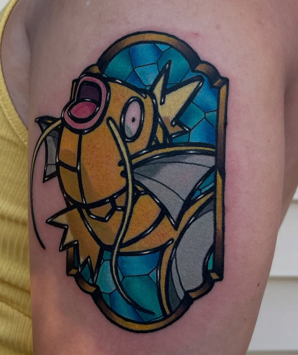 Colorful cartoon turtle tattoo on upper arm featuring blue shell, yellow-orange body, pink open mouth, and gray details with bold black outlines.
