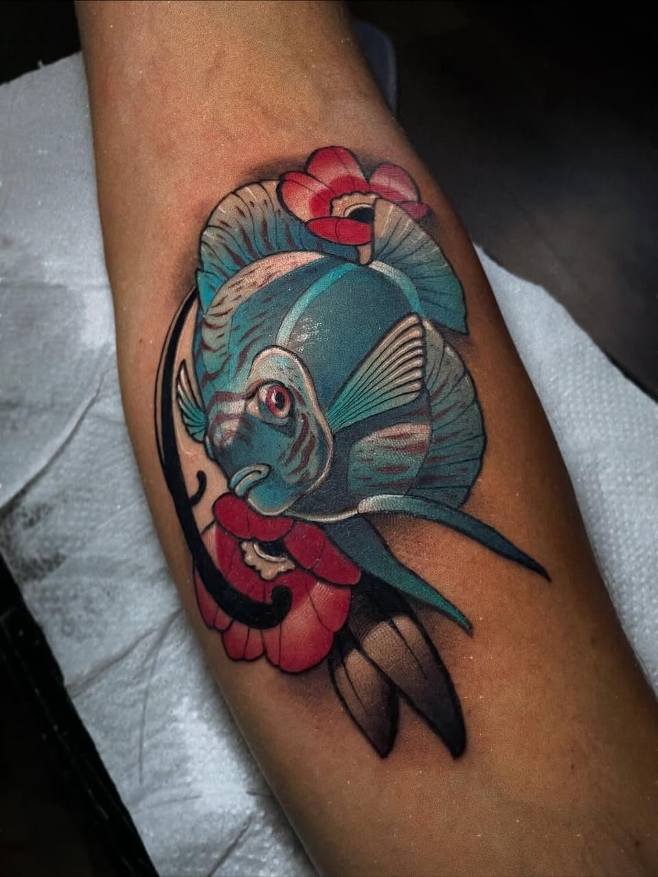 Colorful fish tattoo on the calf featuring a teal fish with pink and red flowers, detailed fins, and a pink eye, displayed on skin.
