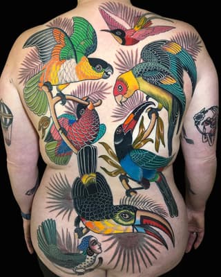Colorful back tattoo featuring multiple parrots and tropical birds perched on branches with spread wings in vibrant greens, yellows, reds, and blues.