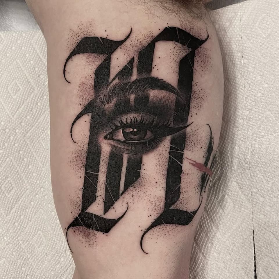 Surreal eye and face tattoo with curved horns, geometric striping, and dotwork shading on the upper thigh in black ink.