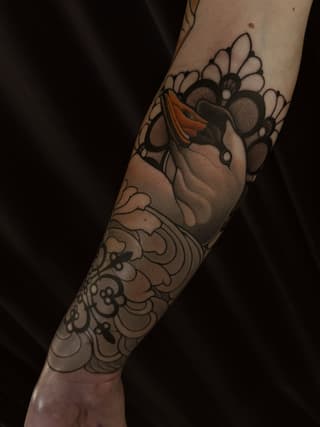 Anatomical heart with orange accents surrounded by daisies and ornamental floral patterns on the forearm and wrist.
