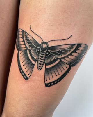 Detailed moth tattoo on upper arm with spread wings, intricate line patterns, and shaded details in black ink on skin.