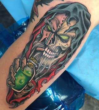 Colored tattoo on forearm featuring a skull with green eyes wearing a red hooded cloak, holding a green glowing orb.