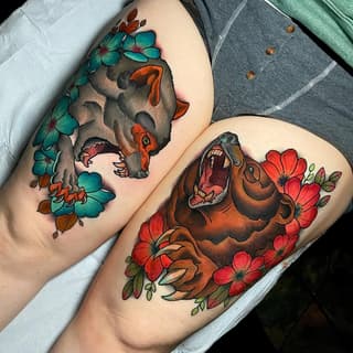 Two thigh tattoos featuring fierce bear heads with open mouths, surrounded by turquoise and red flowers with green foliage.