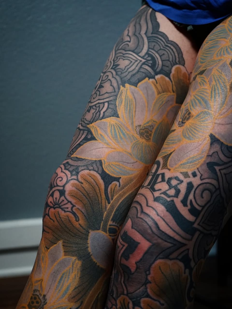Detailed arm tattoos featuring golden flowers with dark ornamental patterns and geometric designs covering both forearms and upper arms.