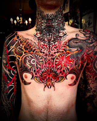 Elaborate red, black, and gold chest and neck tattoo featuring symmetrical ornamental designs with mythical creatures and intricate scrollwork.