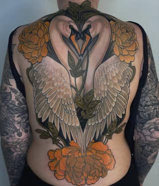 Back tattoo featuring two swans with white wings forming a heart shape, orange peonies, green foliage, and matching orange floral designs on the shoulders.
