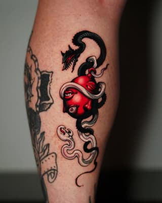 Red and black demon face tattoo with serpents and tentacles on a calf, featuring detailed eyes and ornamental swirling elements below.