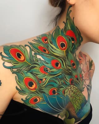 Colorful peacock feather tattoo covering the shoulder and upper back with vibrant green, red, yellow, and blue hues.