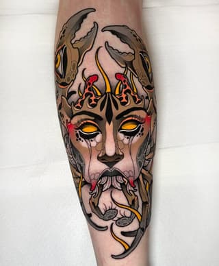 Demonic face tattoo with horns, glowing yellow eyes, red and flame details, and claw hands on a calf in vibrant colors.