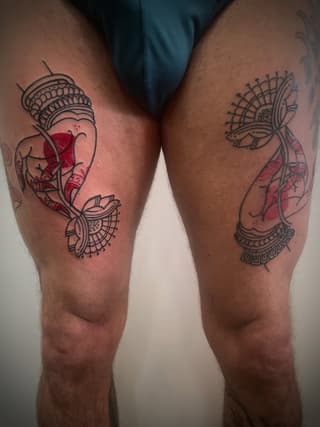 Matching leg tattoos featuring ornate fan designs with red watercolor accents and decorative linework on both thighs.