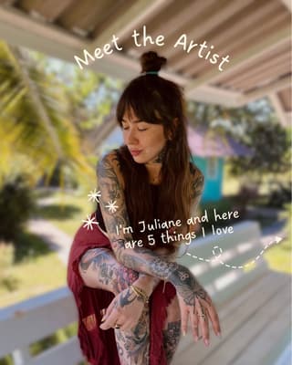 Tattooed woman with extensive arm and leg tattoos in black and colored ink featuring various designs, wearing a burgundy wrap in an outdoor garden setting.