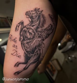 Rearing horse with saddle and rider in grayscale ink on upper arm, accompanied by cursive text reading "Ride or Die.