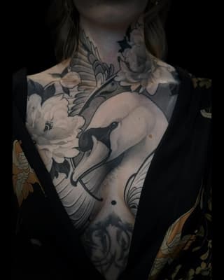 Chest and torso tattoo featuring an elephant with a white flower, decorative scrollwork, and wing designs in black and grey ink with gold accents on the arms.