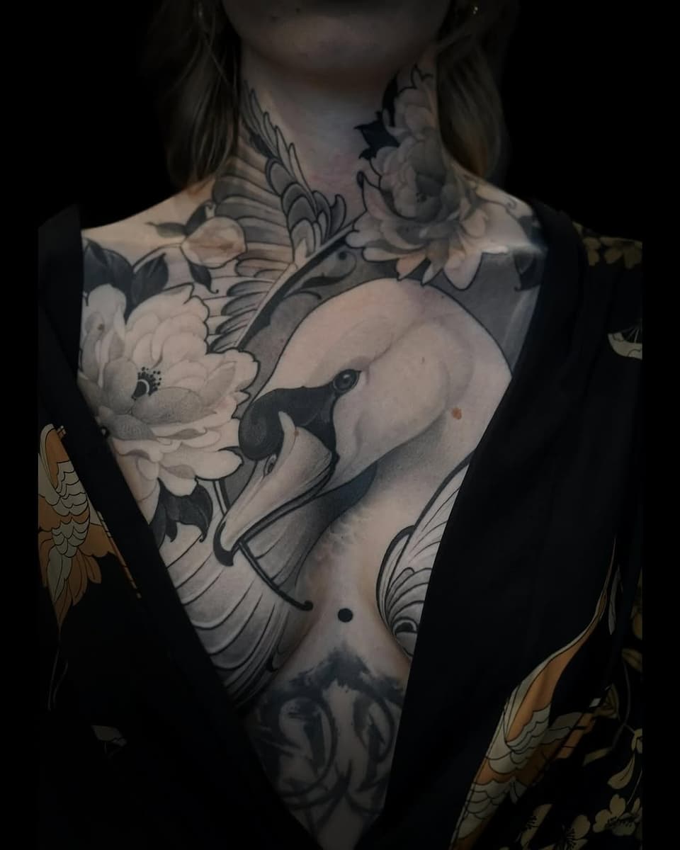Chest and torso tattoo featuring an elephant with a white flower, decorative scrollwork, and wing designs in black and grey ink with gold accents on the arms.