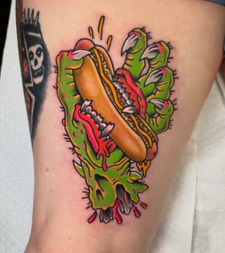 Colorful hot dog and cactus tattoo on upper thigh featuring bright greens, oranges, reds, and yellows with detailed linework.