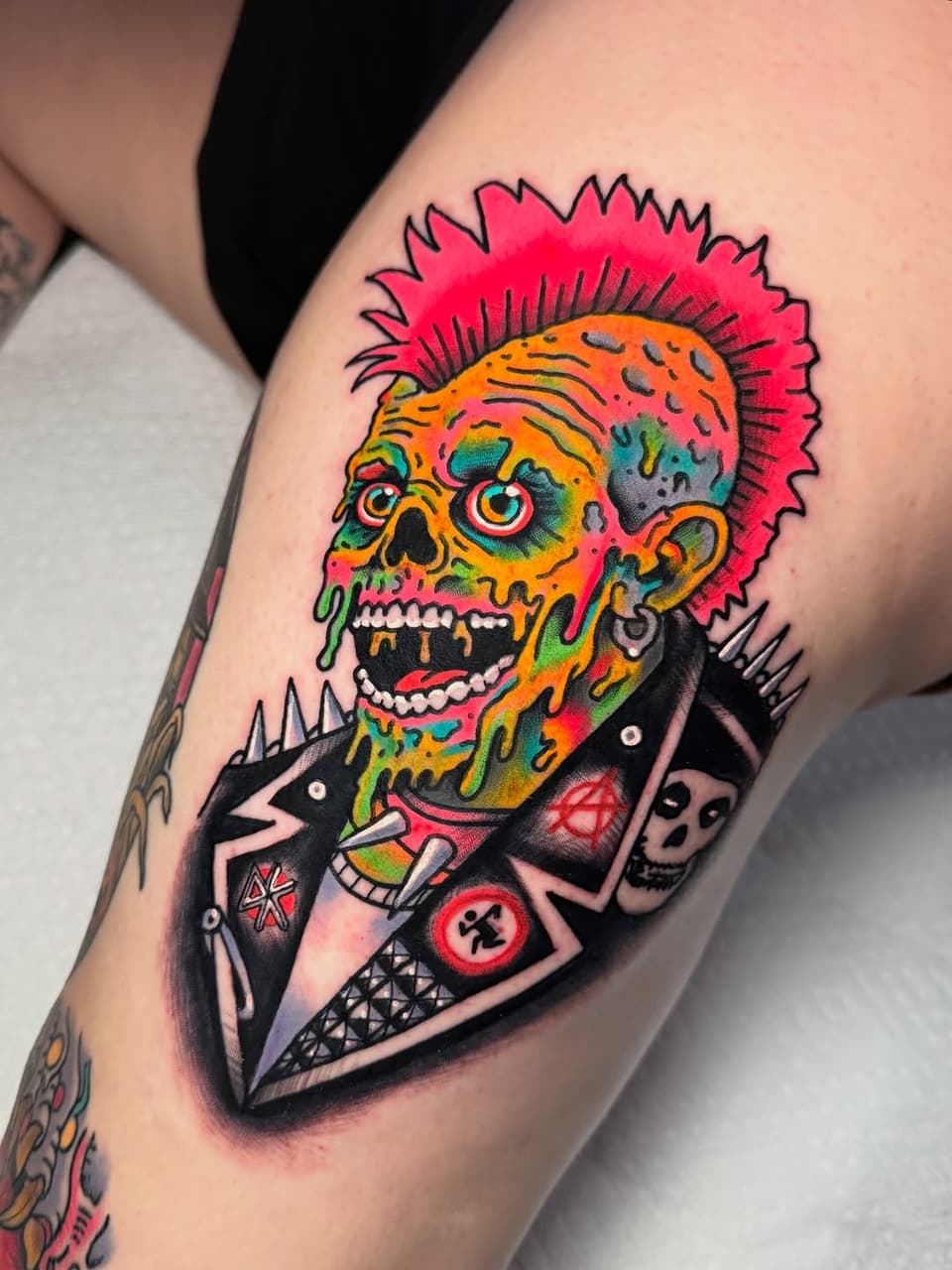 Colorful skull with pink spiky hair wearing a black studded jacket on an upper arm, featuring bright orange, green, and red tones.