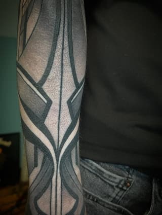 Geometric wing design tattoo on forearm with black, grey, and white lines forming symmetrical angular patterns.
