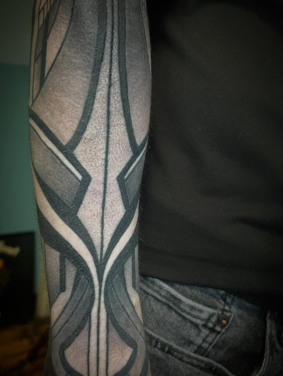Geometric wing design tattoo on forearm with black, grey, and white lines forming symmetrical angular patterns.