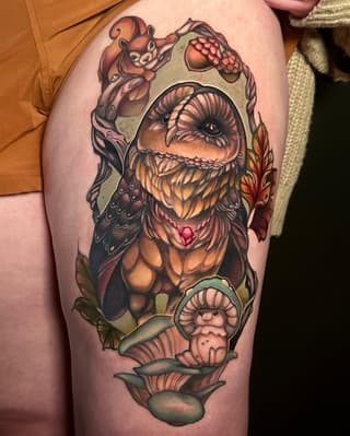 Colorful thigh tattoo featuring a large bearded creature with a heart on its chest, surrounded by smaller characters, mushrooms, and foliage in orange, brown, and green tones.