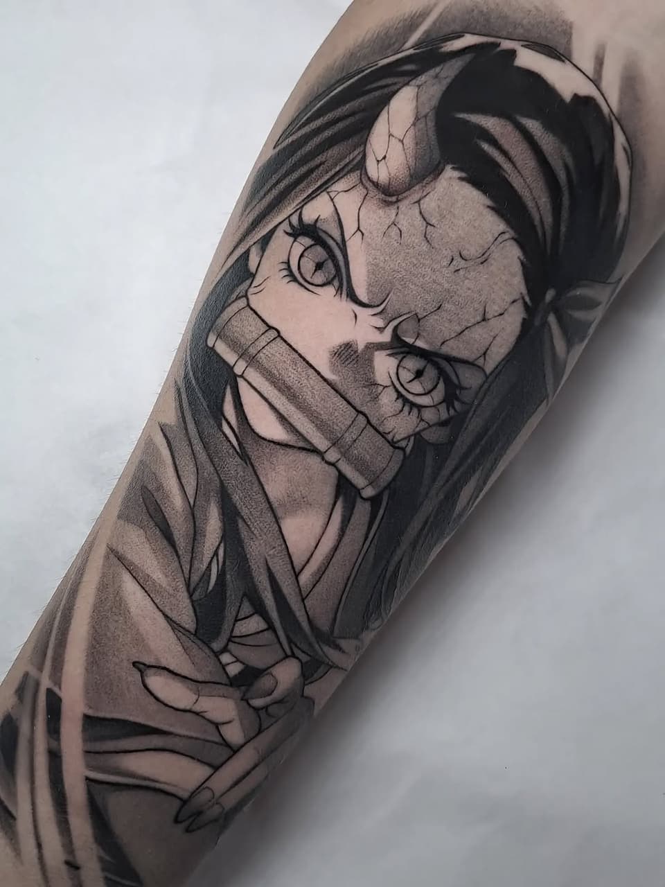 Tattoo on forearm depicting a character with closed eyes, headwrap, and detailed facial features in black and gray ink.