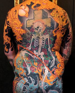 Full back tattoo featuring a skeleton with a cross, surrounded by red roses, orange flames, and ornamental designs in vibrant colors.