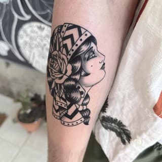 Profile of a woman's head with wavy hair, flower, and geometric patterns on her arm in black ink.