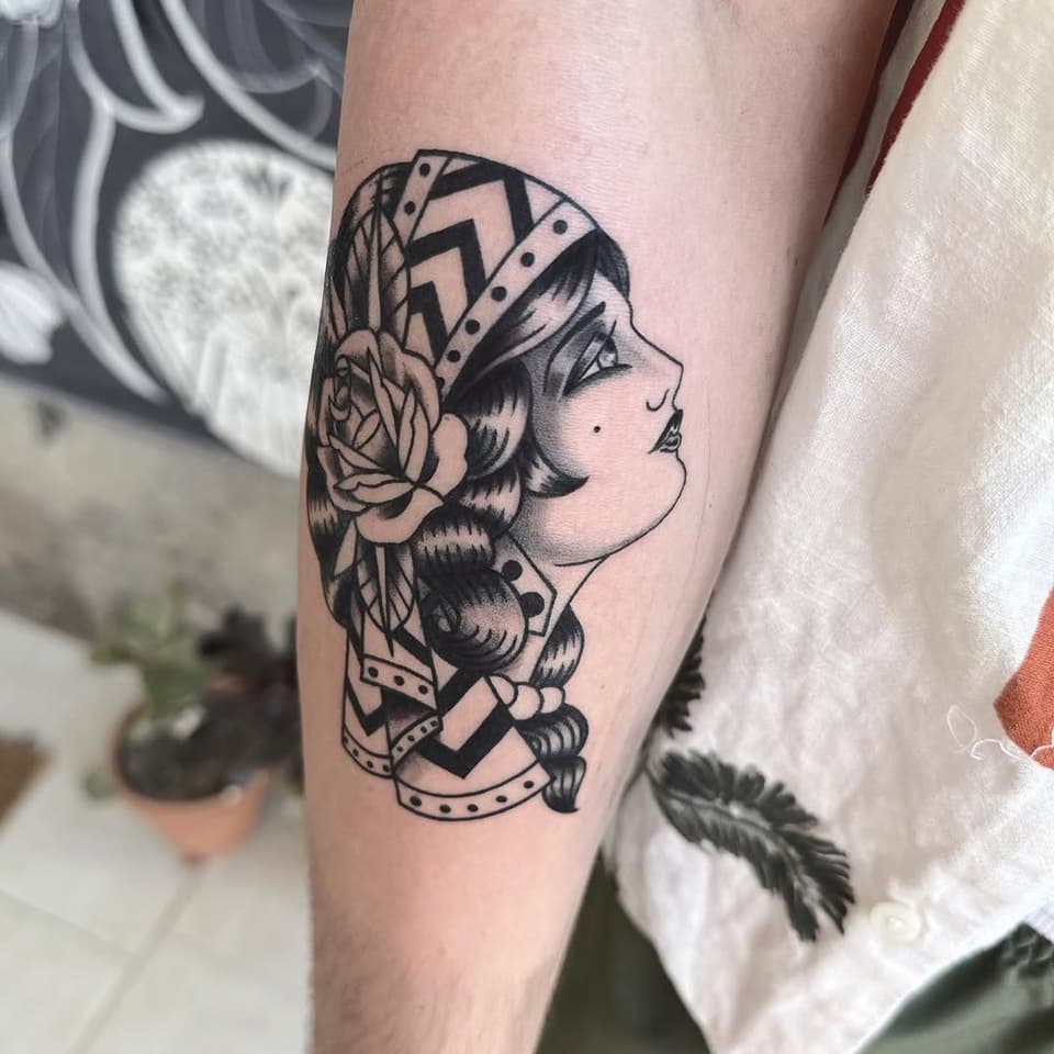 Profile of a woman's head with wavy hair, flower, and geometric patterns on her arm in black ink.