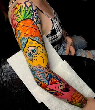 Colorful leg sleeve tattoo featuring a yellow character with large eyes, pineapple, strawberries, and red creature with text, displayed on white paper.